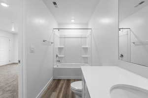 Bathroom with vanity, toilet, tub / shower combination, baseboards, and wood finished floors