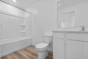 Full bathroom with toilet, vanity, washtub / shower combination, wood finished floors, and baseboards
