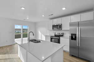 Kitchen featuring stainless steel appliances, a sink, light wood-style floors, white cabinets, and a center island with sink