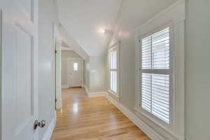 Hall featuring light wood-style floors, baseboards, and lofted ceiling