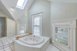 Bathroom with a skylight, lofted ceiling, a jetted tub, and tile patterned flooring