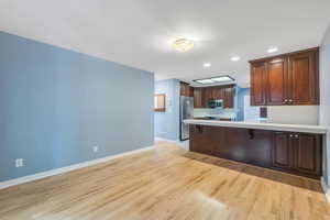 Kitchen featuring stainless steel appliances, light countertops, a peninsula, light wood-style flooring, and baseboards