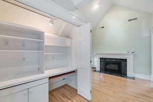 Unfurnished office featuring light wood-style flooring, vaulted ceiling, a fireplace, and baseboards