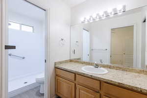 Bathroom featuring toilet, vanity, and a shower