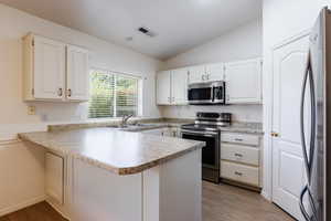 Kitchen featuring appliances with stainless steel finishes, a sink, a peninsula, lofted ceiling, and light wood-type flooring
