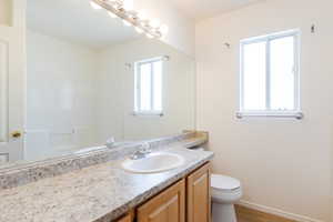 Bathroom with vanity, toilet, wood finished floors, baseboards, and a shower