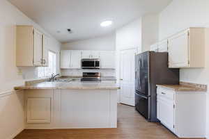 Kitchen with appliances with stainless steel finishes, a sink, lofted ceiling, a peninsula, and light wood-style flooring