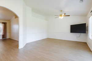 Unfurnished living room featuring arched walkways, a ceiling fan, healthy amount of natural light, lofted ceiling, and light wood finished floors