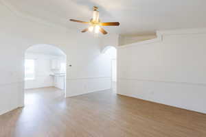 Spare room featuring arched walkways, a ceiling fan, light wood-type flooring, crown molding, and baseboards