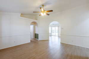 Empty room with arched walkways, a ceiling fan, light wood-style flooring, ornamental molding, and baseboards