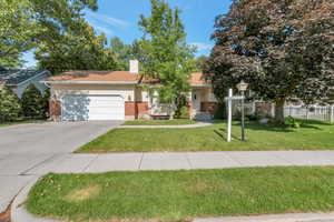 View of property hidden behind natural trees with a garage, concrete driveway, a chimney, with  brick siding