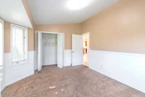 Unfurnished bedroom with lofted ceiling, wainscoting, a closet, carpet floors, and a textured ceiling