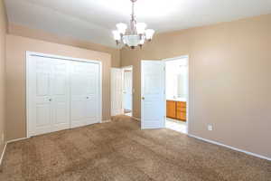 Unfurnished bedroom featuring a chandelier, light carpet, a closet, and suite bath