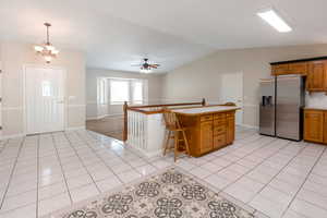Kitchen with stainless steel refrigerator with ice dispenser, light countertops, a ceiling fan, light tile patterned flooring, and lofted ceiling