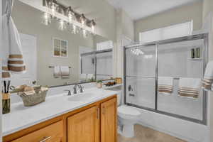 Full bathroom featuring toilet, vanity, bath / shower combo with glass door, and tile patterned flooring