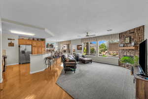 Living area featuring a textured ceiling, light wood finished floors, a ceiling fan, and baseboards