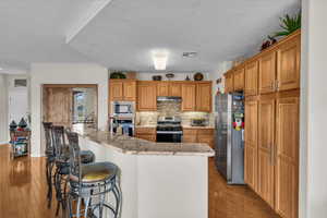 Kitchen featuring appliances with stainless steel finishes, under cabinet range hood, a breakfast bar, light wood-type flooring, and a textured ceiling