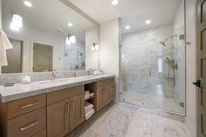 Bathroom with recessed lighting, marble look tiles, double vanity, and a marble finish shower