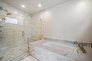 Bathroom featuring a bath, a marble finish shower, and recessed lighting