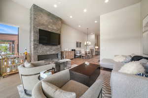 Living area with light wood finished floors, a stone fireplace, recessed lighting, and a chandelier