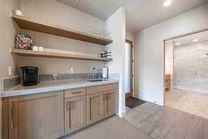 Bar with a sink, recessed lighting, light marble finish floors, and baseboards