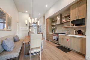 Kitchen with wall chimney range hood, premium stove, black microwave, open shelves, and a sink