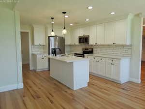 Updated kitchen with stainless steel appliances, baseboards, light wood-style flooring, decorative backsplash, and white cabinetry