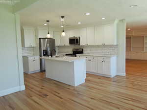 Updated kitchen with stainless steel appliances, a sink, light wood finished floors, white cabinets, and recessed lighting in an open floorplan layout