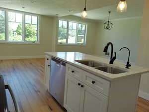 Updated kitchen island featuring stainless steel dishwasher, a sink, decorative light fixtures, white cabinetry, and light quartz countertops