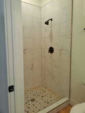Bathroom featuring a tile shower, toilet, and wood finished floors