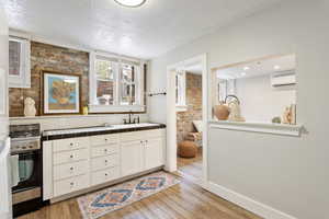 Kitchen featuring a sink, stainless steel gas stove, a wall mounted AC, tile countertops, and light wood finished floors