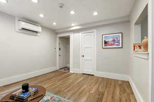 Below grade area featuring a wall unit AC, light wood-style floors, baseboards, and recessed lighting