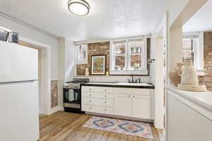 Kitchen with stainless steel gas stove, freestanding refrigerator, light wood-style flooring, a textured ceiling, and a sink