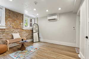 Sitting room featuring a wall mounted AC, baseboards, light wood finished floors, recessed lighting, and brick wall