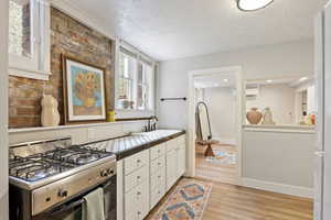 Kitchen with range with gas cooktop, a sink, a textured ceiling, tile countertops, and white cabinets