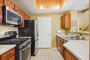Kitchen featuring stainless steel appliances, a sink, light tile patterned flooring, and brown cabinetry