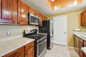 Kitchen with stainless steel appliances, light countertops, light tile patterned floors, and brown cabinetry