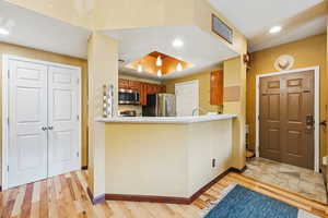 Kitchen with stainless steel appliances, brown cabinets, baseboards, light wood-style flooring, and a peninsula