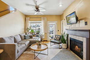 Living room featuring a tiled fireplace, wood finished floors, and ceiling fan