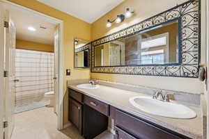Bathroom with toilet, double vanity, a shower with curtain, and baseboards