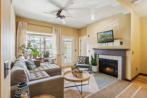 Living area with wood finished floors, a tile fireplace, ceiling fan, and baseboards