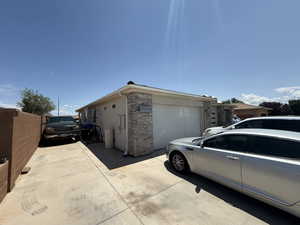 View of side of property featuring stone siding, a garage, stucco siding, and concrete driveway