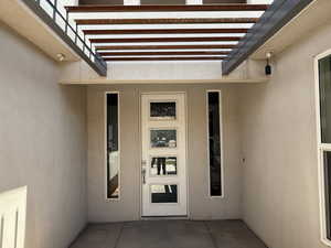 Doorway to property with stucco siding and a pergola