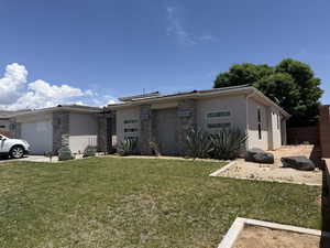 View of front of property with an attached garage, stucco siding, stone siding, and a front yard