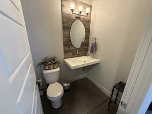 Bathroom with toilet, concrete flooring, and baseboards