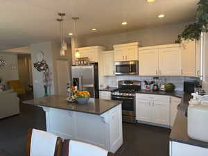 Kitchen featuring stainless steel appliances, dark countertops, decorative backsplash, white cabinetry, and recessed lighting