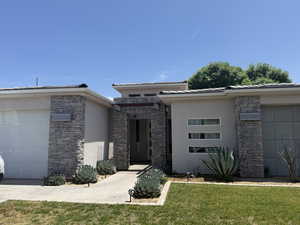 View of front of house with stucco siding, stone siding, a front yard, and a garage