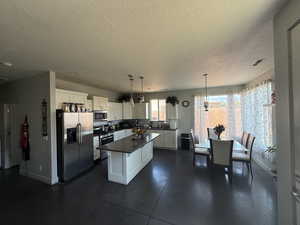 Kitchen with stainless steel appliances, a textured ceiling, dark countertops, white cabinets, and a kitchen island