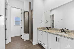 Primary Bathroom with a tile stall shower, baseboards, double vanity, and LVP finished floors
