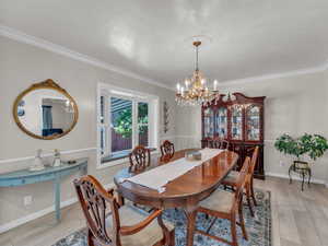 Dining area with a chandelier, crown molding, light wood-style flooring, and baseboards